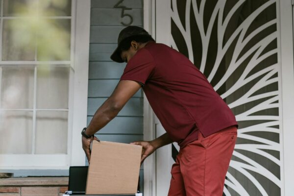 Courier picking up a cardboard package from a doorstep - e-commerce delivery and returns